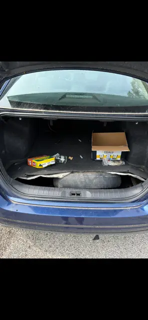 Sedan trunk with loose packaging, debris and dirt worked into the carpet