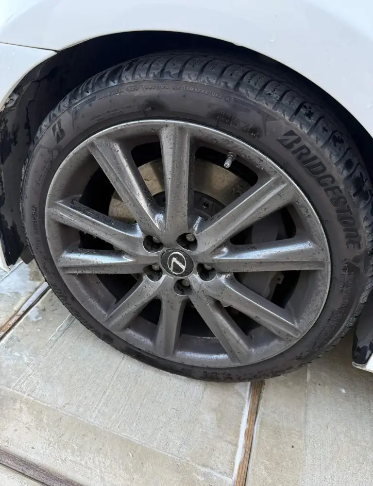Lexus alloy wheel coated in brake dust and road grime, tire wall dull and brown