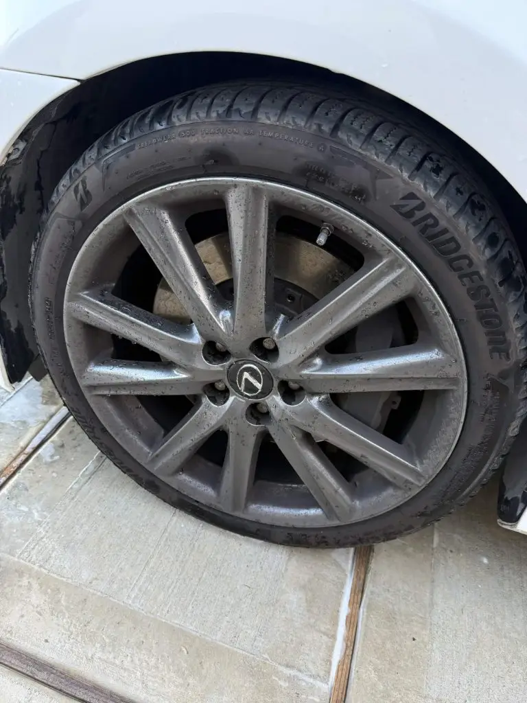 Lexus alloy wheel coated in brake dust and road grime, tire wall dull and brown